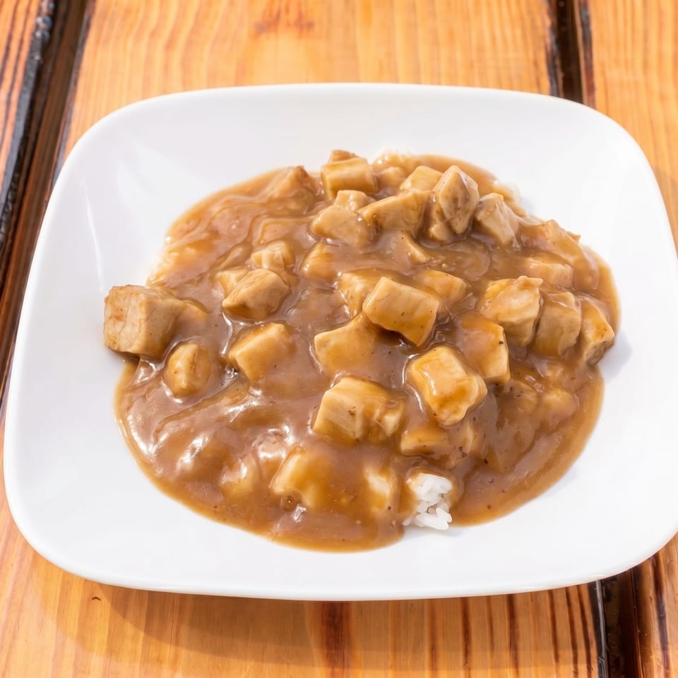A white plate holds a serving of chicken curry with rice on a wooden table.