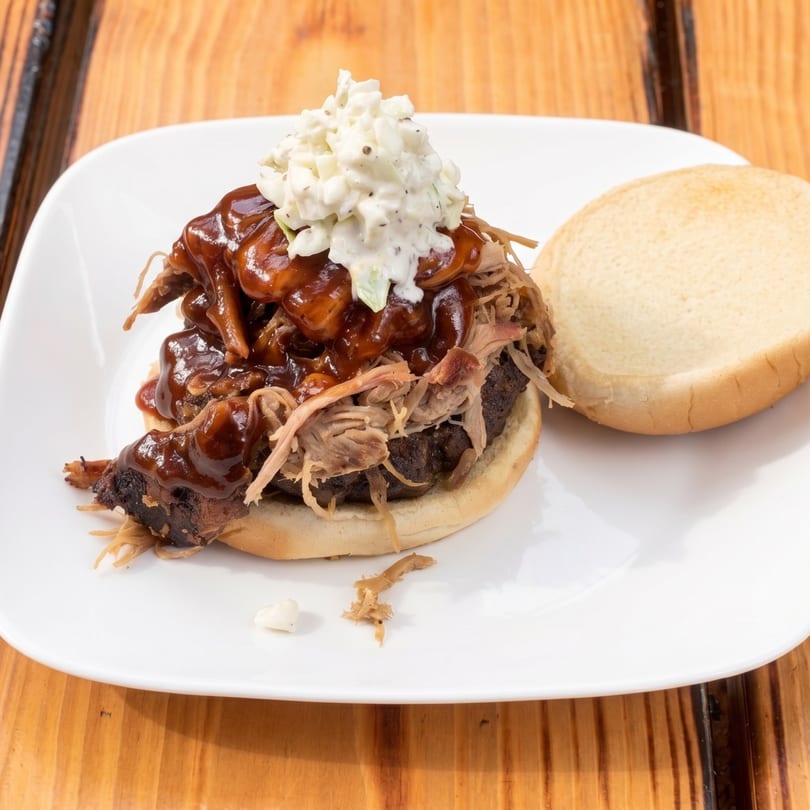 Pulled pork sandwich with barbecue sauce and coleslaw on a white plate with an open bun.