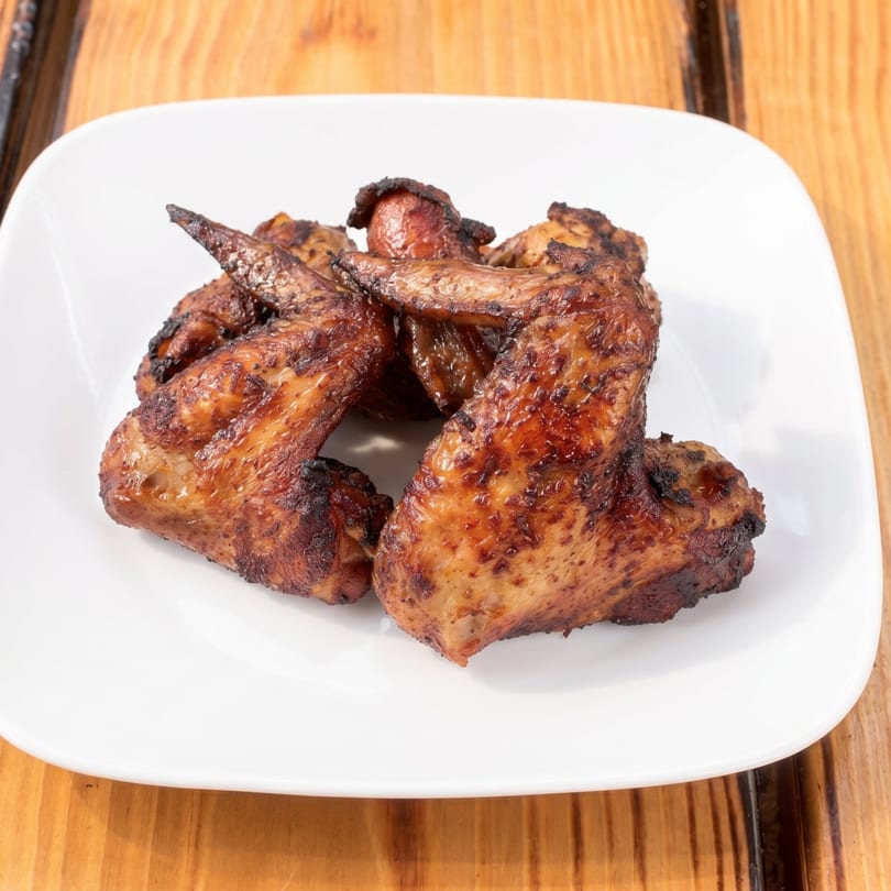A white plate holds several crispy, golden-brown chicken wings on a wooden table.